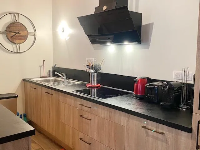 Une cuisine entièrement équipée avec lave vaisselle, plaque induction, four, cafetières, réfrigérateur et congélateur, et ouverte sur la pièce principale par un bar avec chaises hautes