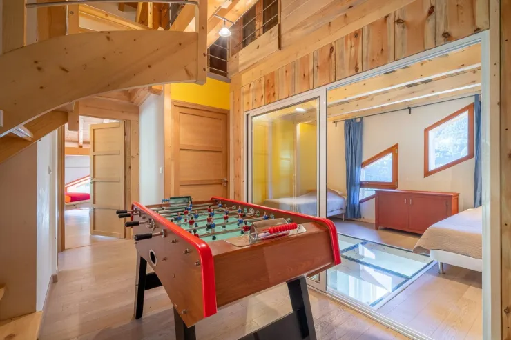 La salle de distribution des chambres accueille le babyfoot et le sauna. On voit l'espace couchage (salon supplémentaire) avec sa porte vitrée et les pavés de verre qui donnent sur le salon.