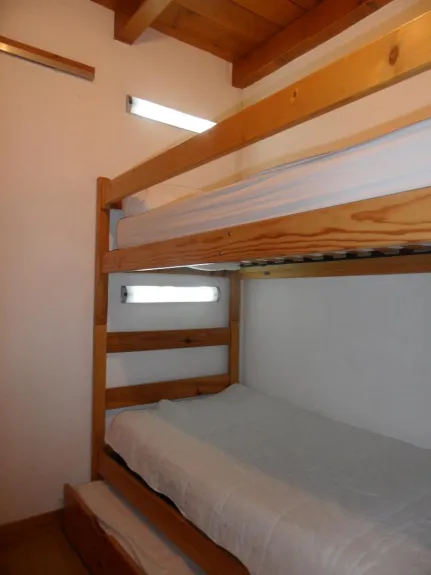 La chambre avec 3 couchages individuels avec éclairage fixe. Une penderie rangement avec portes coulissantes et une colonne de rangement au bout des lits.