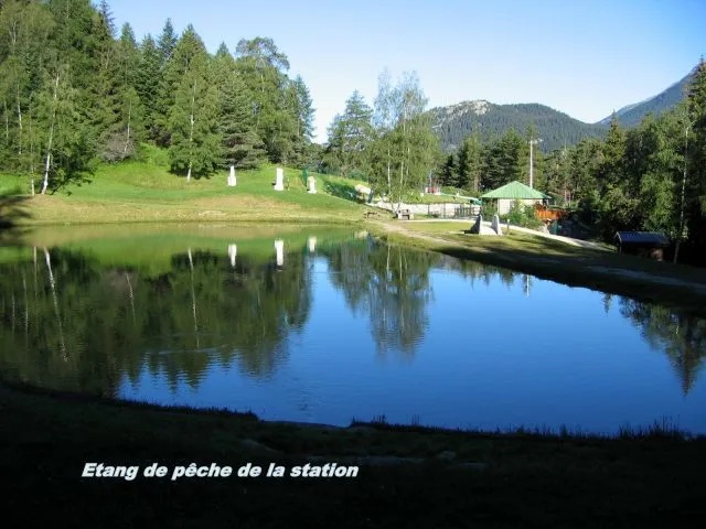 l'Etang de pêche de la station, avec les aménagement table banc et grille barbecue, pêche à la truite, carte disponible à l'office du tourisme de la station, à l'arrière la piscine de plein air surveillé en saison,