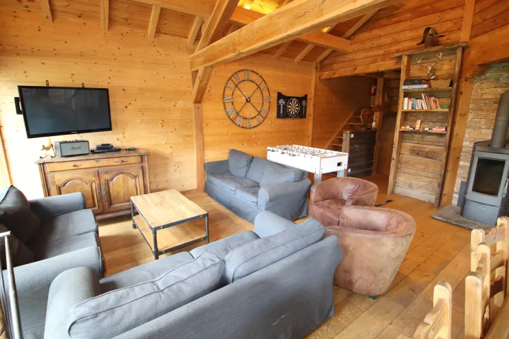 Large living room under a cathedral ceiling in Chalet B in Vars with wood-burning stove, U-shaped sofa, flat screen TV, foosball table and darts.
