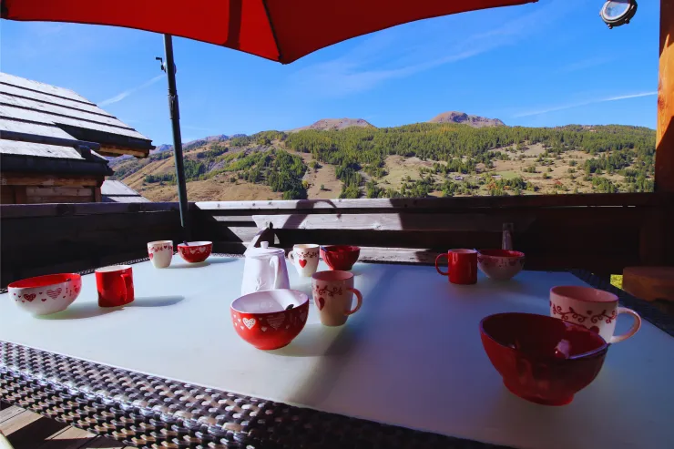 Outdoor table set for breakfast on the terrace of Chalet B in Vars, at the level of the kitchen and living room, with the mountain in the background.