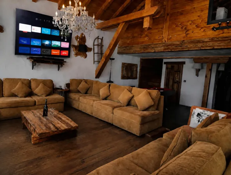Living room at Le Soleil Chalet in Montgenèvre: large sofas, exposed wooden beams, crystal chandelier, and a mezzanine
