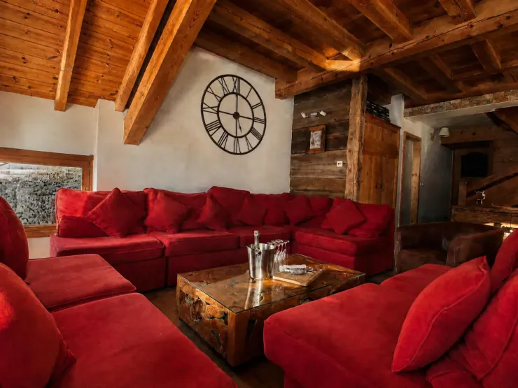 Vaste salon du Chalet C à Vars avec un grand canapé en U rouge, une table basse en verre et des murs revêtus de vieux bois authentique.